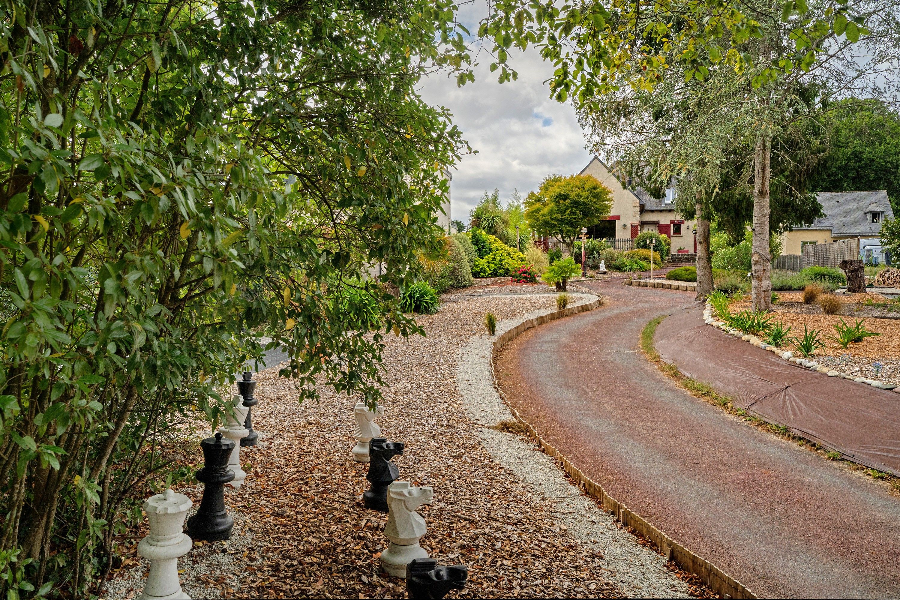 Rua residencial com estrada sinuosa, cercada por árvores e uma casa com telhado inclinado.