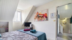 Un dormitorio con una cama, un escritorio con una computadora, un cuadro y una puerta que da a un pasillo.