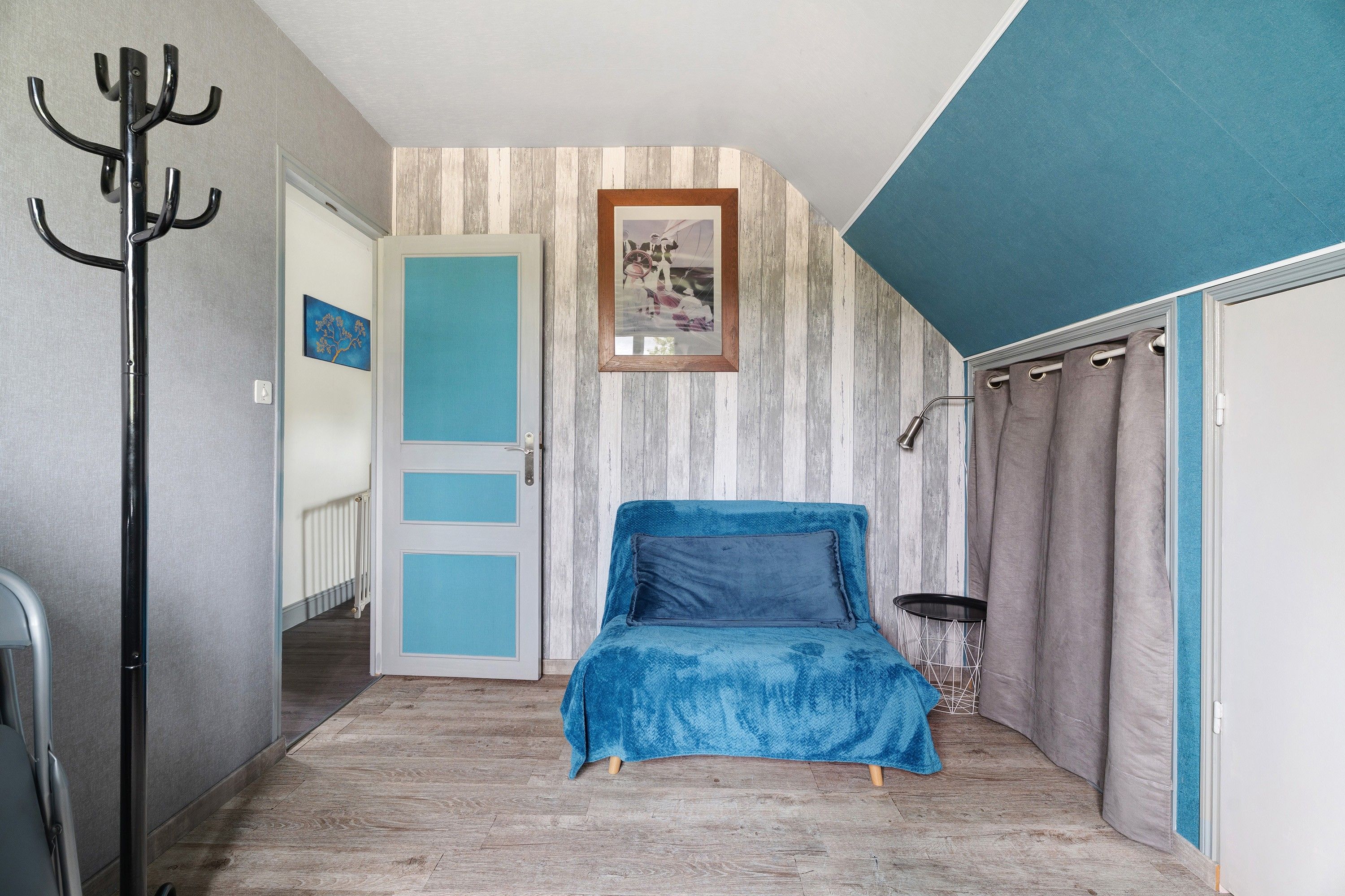 A bedroom with a bed, a coat rack, a door, and a wall with a picture.