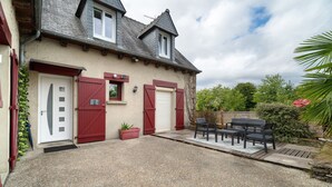 Una casa de dos pisos con entrada de grava, una puerta roja y un patio con mobiliario exterior.