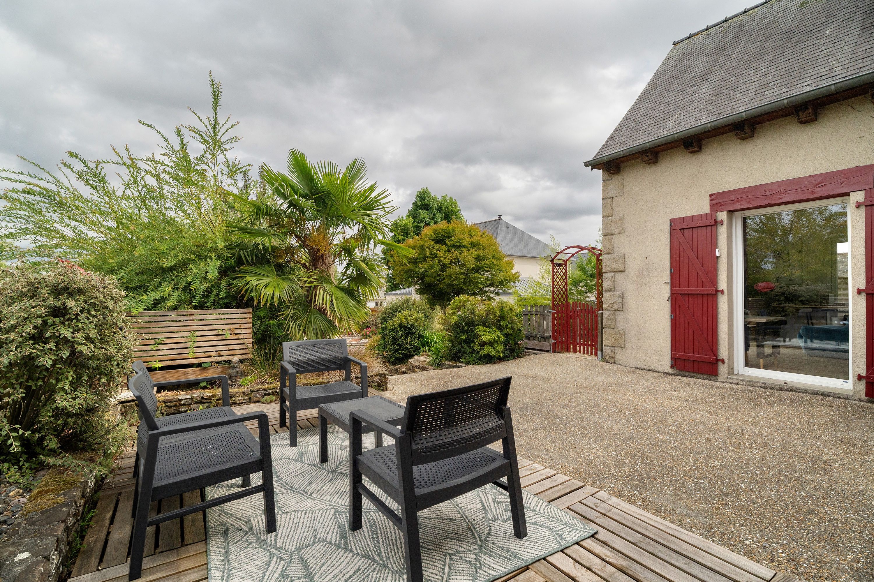 An outdoor patio area with a gravel surface, two black metal chairs, a wooden bench, and a red gate.