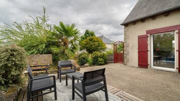 An outdoor patio area with a gravel surface, two black metal chairs, a wooden bench, and a red gate.