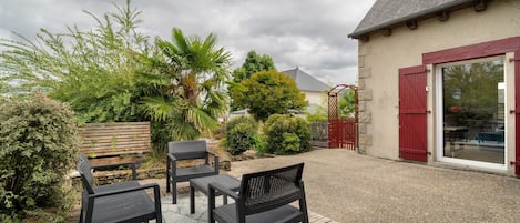 An outdoor patio area with a gravel surface, two black metal chairs, a wooden bench, and a red gate.