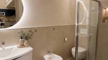 Un baño moderno con un tocador curvo, un bidé, un inodoro y una ducha con cerramiento de vidrio.