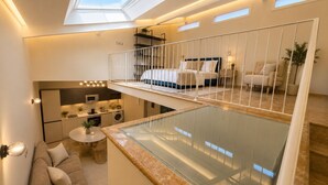 Un apartamento moderno con balcón de vidrio, cocina, comedor y dormitorio con cama y mesita de noche.