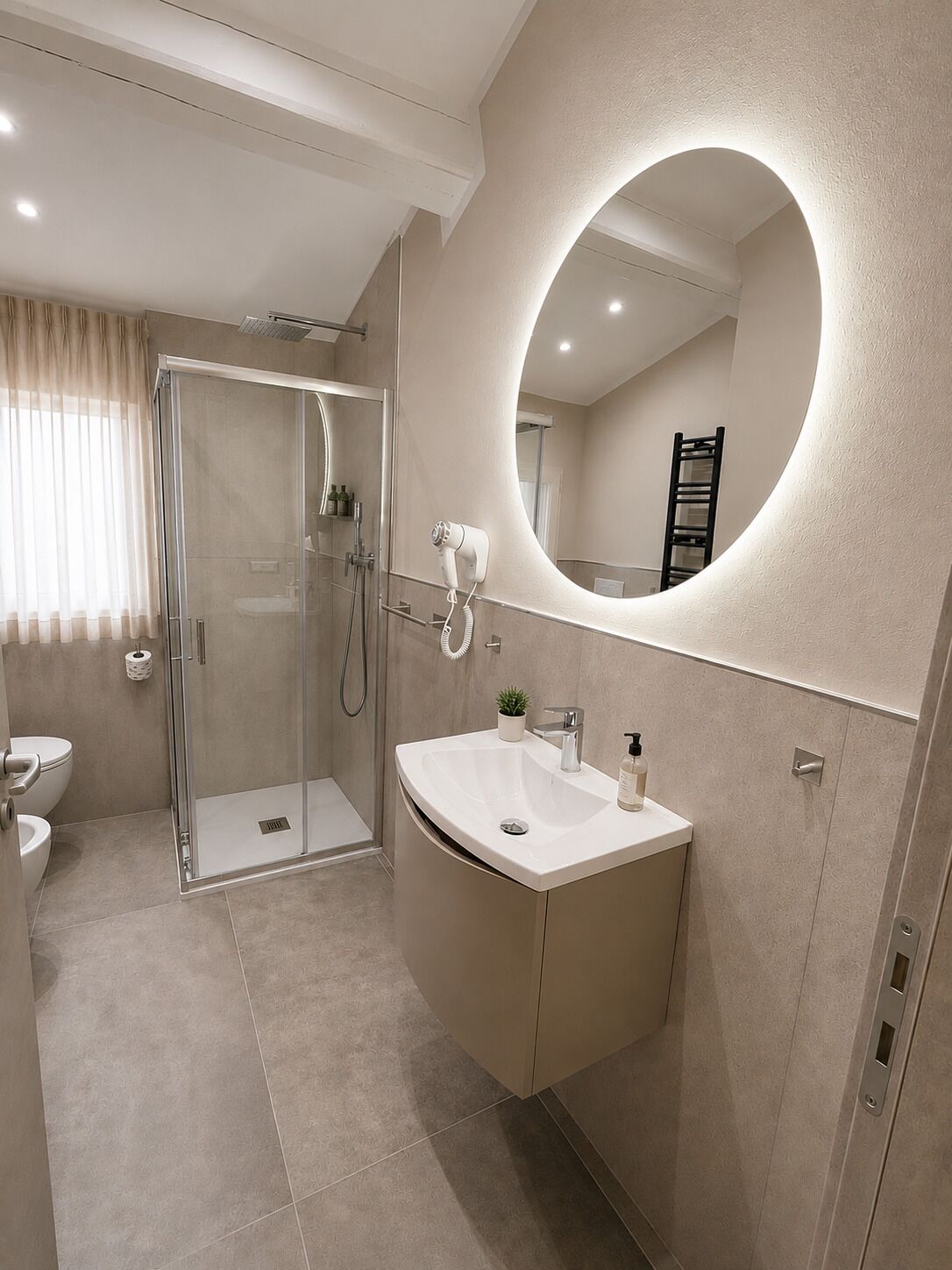 A modern bathroom with a glass shower enclosure, a vanity with a sink, and a large mirror with a circular frame.