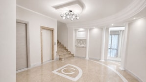Un pasillo amplio con piso de mármol, una escalera y un elegante candelabro.