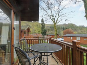 Eine Holzterrasse mit rundem Tisch und Stühlen, mit Blick auf eine Wohngegend mit Häusern und Bäumen.