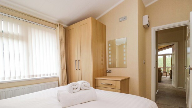 A hotel room with a bed, a wooden wardrobe, a bedside table, a mirror, and a view of a balcony. - Wally's Folly (Windermere)
