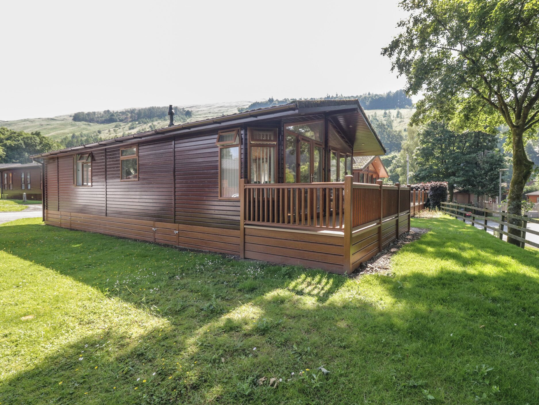 A wooden cabin with a deck, surrounded by grass and trees.