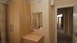 A bedroom with a wooden wardrobe, a small bedside table, a mirror, and a door leading to a balcony. - Wally's Folly (Windermere)