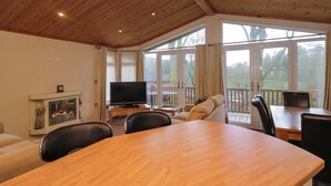 A wooden ceiling, a television on a wooden stand, a dining table, and a sofa. - Wally's Folly (Windermere)