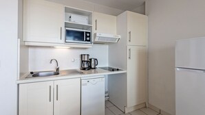 Cocina compacta con alacenas blancas, microondas, cafetera, lavavajillas y refrigerador.