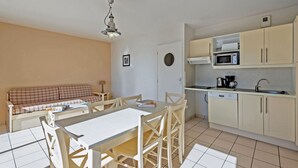 A compact kitchen with a microwave, stove, and sink. There is a dining table with chairs and a sofa in the living area. - Balcon avec vue sur mer | Appt 6p + Accès  sauna (Plougonvelin)