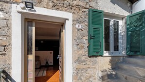 A stone building with a wooden door, a window with green shutters, and a staircase leading to the entrance.