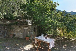 A rustic outdoor dining area with a stone wall, wooden table, and chairs, surrounded by greenery and a mountain view. - Casa Vacanze Luce in Castelbianco – Tranquillity in Nature (Oresine)