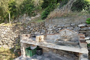 A stone wall with a stone bench and a small stone structure, possibly a fireplace, in a natural setting.