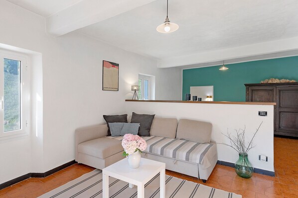 A living room with a sofa, a white table, a vase with flowers, a green wall, and a kitchen area in the background. - Casa Vacanze Luce in Castelbianco – Tranquillity in Nature (Oresine)