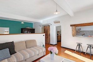 A living room with a sofa, a coffee table with a vase, and a kitchen area in the background.