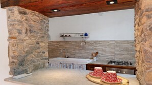 A kitchen with a stone wall, a sink, a stove, and a tray with cups.