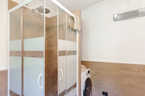 Ein modernes Badezimmer mit einer Glaskabine zur Dusche, einer integrierten Waschmaschine und einer Holzvertäfelung.