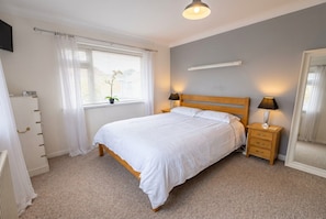 Une chambre à coucher avec un lit, des tables de chevet, une fenêtre avec des rideaux, un radiateur et un miroir.
