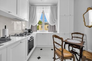 Une cuisine moderne avec des meubles blancs, une table à manger avec des chaises et une vue par une fenêtre agrémentée de rideaux.