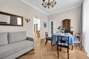 Un salon comprenant un canapé, une table à manger avec des chaises, un lustre et un meuble en bois.