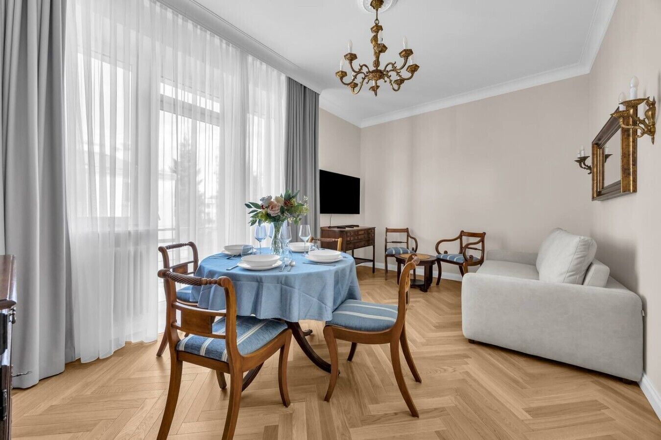 Een eetgedeelte met een ronde tafel, stoelen, een kroonluchter en een bank.