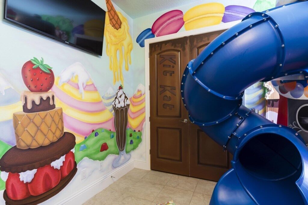 Un área de juegos infantiles con un tobogán, decoraciones de pared coloridas y una puerta con la etiqueta 'KiKi Kiosk'.