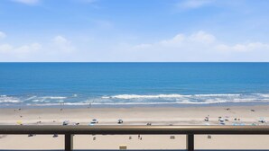 Ein Strand mit blauem Himmel, ruhiger See und einem Geländer im Vordergrund.