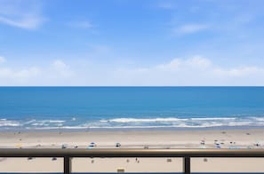 Ein Strand mit blauem Himmel, ruhiger See und einem Geländer im Vordergrund.