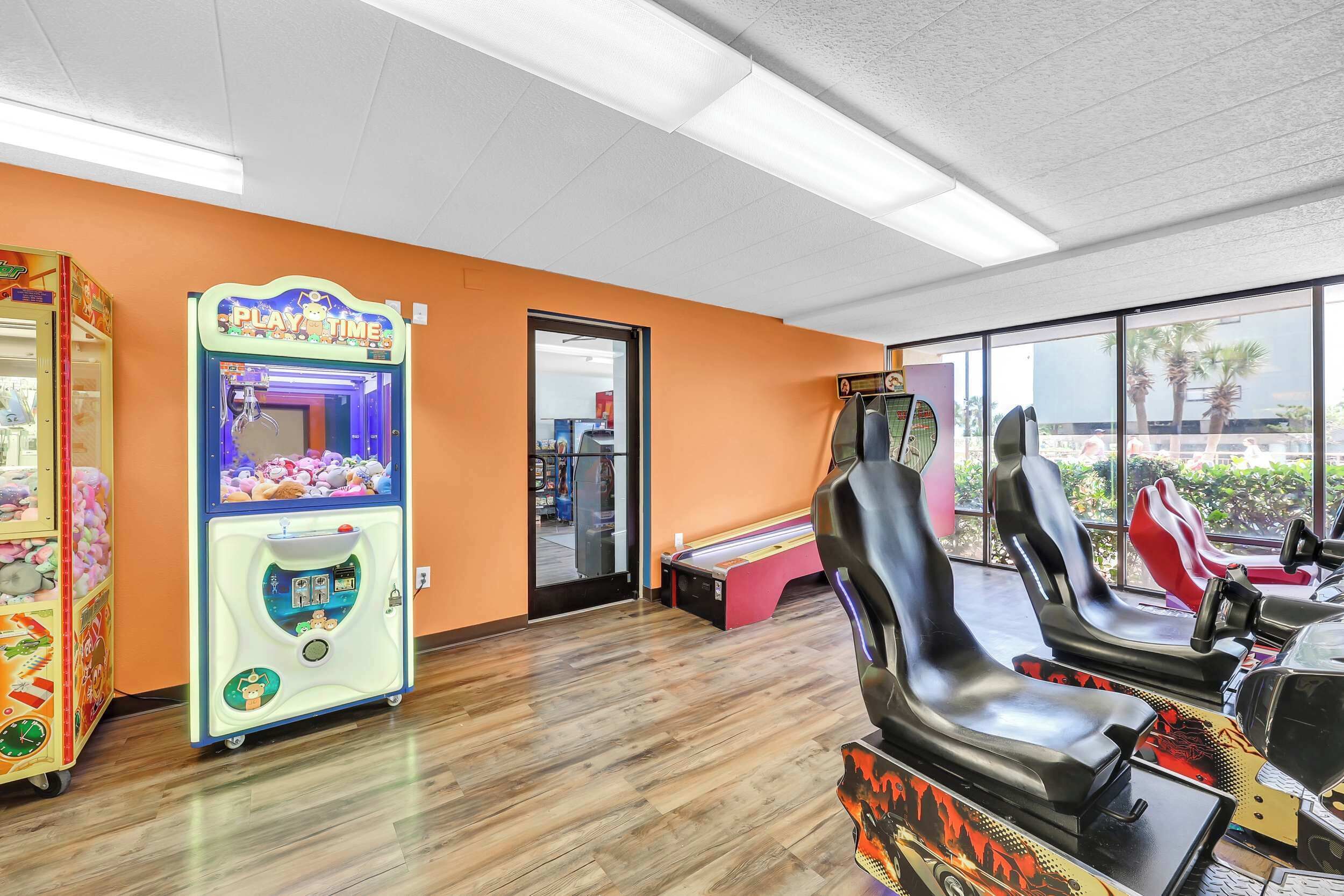 A room with a Play'n'Time claw machine, gaming chairs, and a view through large windows.