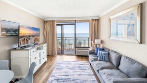 Ein Zimmer mit Fernseher, einer Couch, einem Esstisch und Meerblick durch große Fenster.