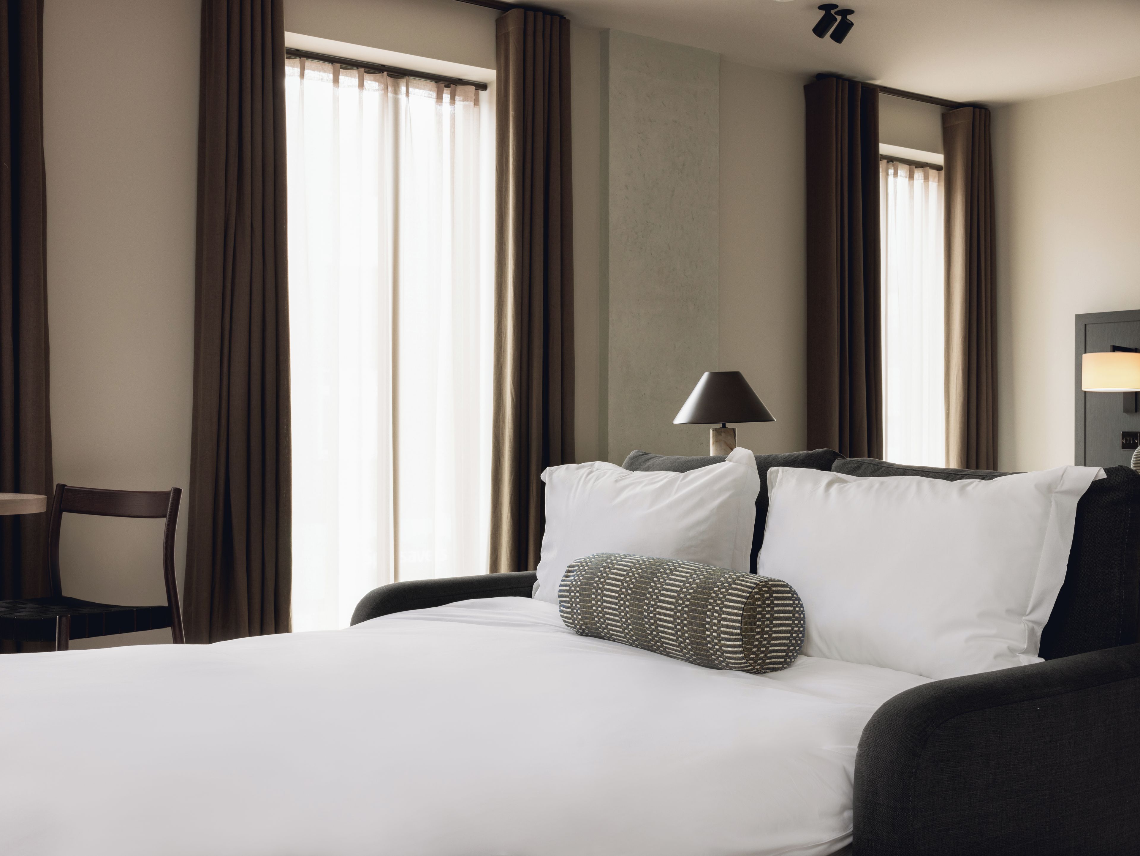 Ein Hotelzimmer mit einem Bett, einem Sessel, einer Lampe und einem Fenster mit Vorhängen.