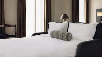 A hotel room with a bed, a chair, a lamp, and a window with curtains.