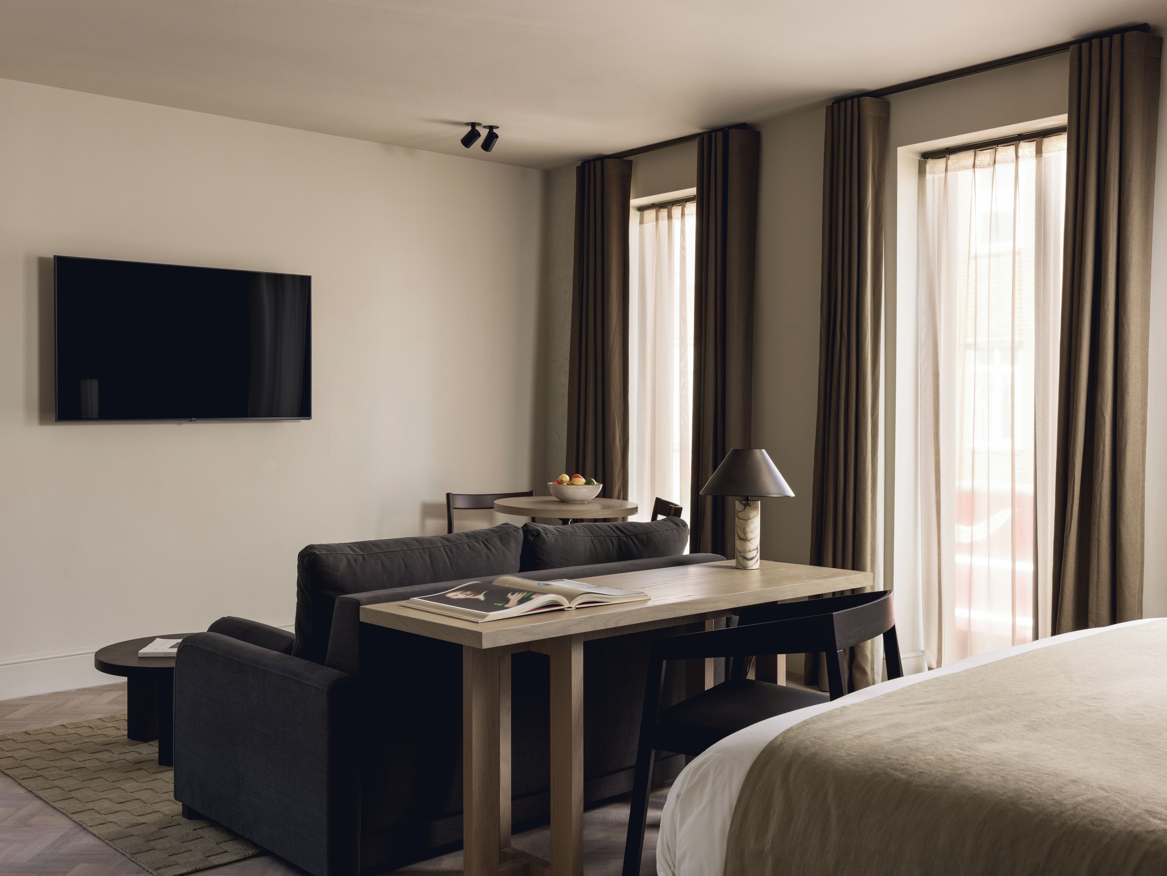 A hotel room with a bed, a desk with a lamp, a sofa, a TV, and curtains.