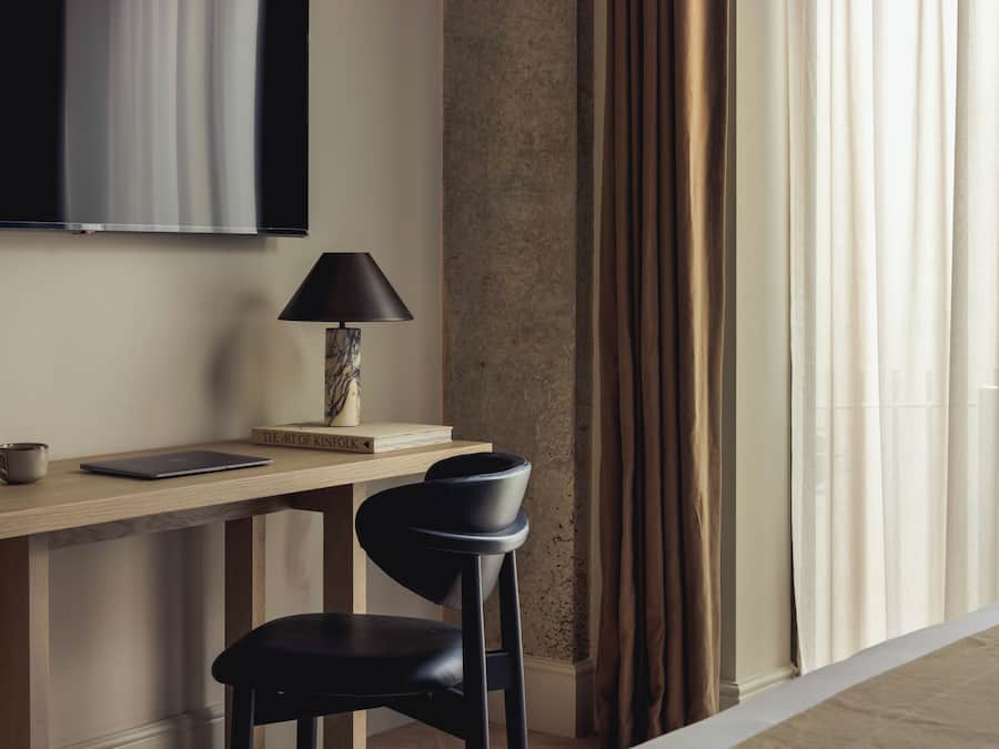A modern room with a wooden desk, a black chair, a lamp, a laptop, and a book titled 'THE ART OF KINFKOLK.'