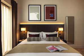 A hotel room with a large bed, two bedside lamps, a nightstand, a mirror, and two framed pictures on the wall. - Native Fulham Broadway (London)