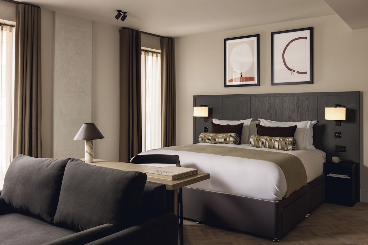 A hotel room with a bed, bedside tables, a desk, a chair, and a window with curtains.