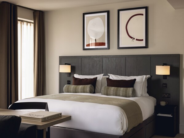 A hotel room with a large bed, two wall-mounted lamps, a framed artwork above the bed, and a nightstand with a cup. - Native Fulham Broadway (London)