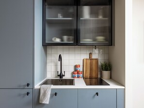 A kitchen with a modern design, featuring a stainless steel sink, a wooden cutting board, and a potted plant. - Native Fulham Broadway (London)