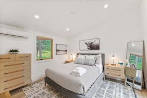 A modern bedroom with a bed, bedside tables, a dresser, a mirror, and artwork on the walls.