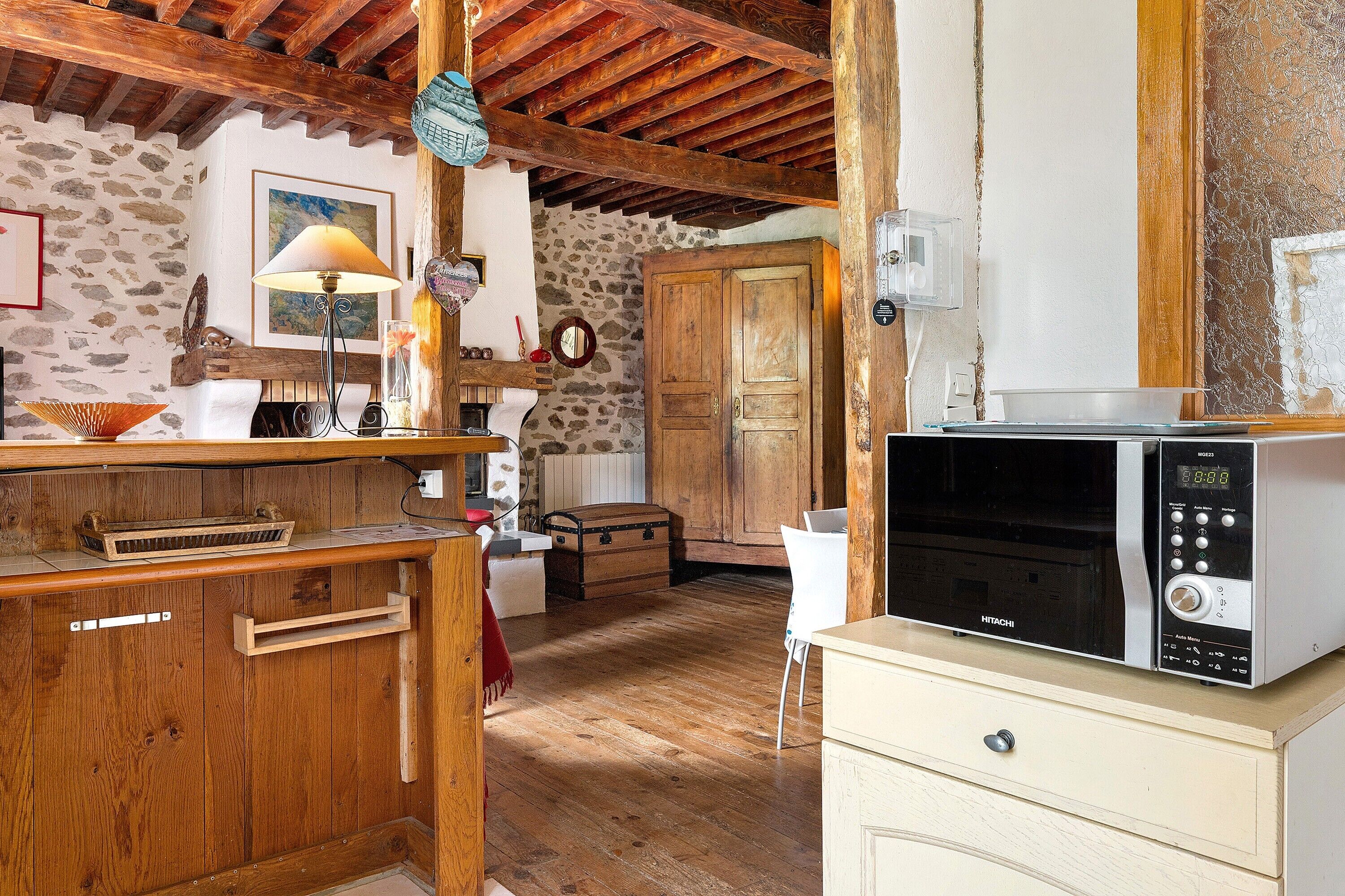A rustic kitchen with wooden cabinets, a microwave, and a stone wall.