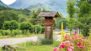 Ein rustikales Holzschild mit der Aufschrift 'Bienvenue Bonac', umgeben von üppiger Vegetation und einem Bergpanorama.