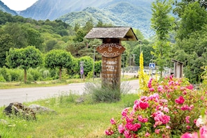 Ein rustikales Holzschild mit der Aufschrift 'Bienvenue Bonac', umgeben von üppiger Vegetation und einem Bergpanorama.