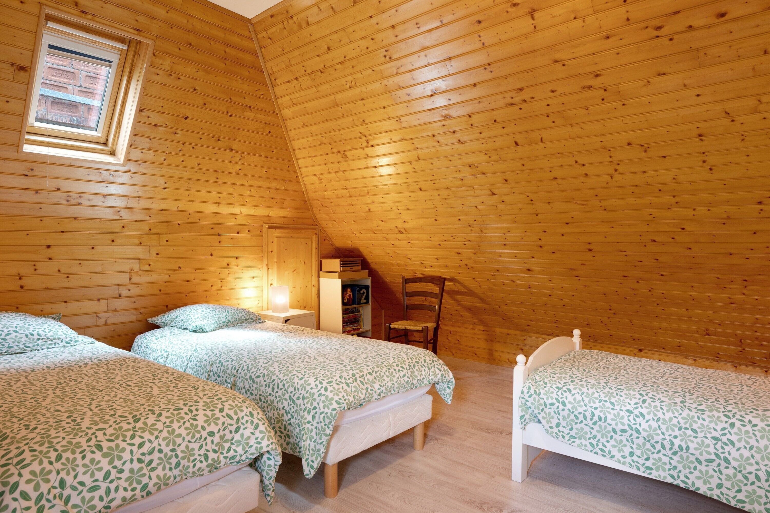 Camera da letto in una baita di legno con tre letti, un lucernario e una libreria.