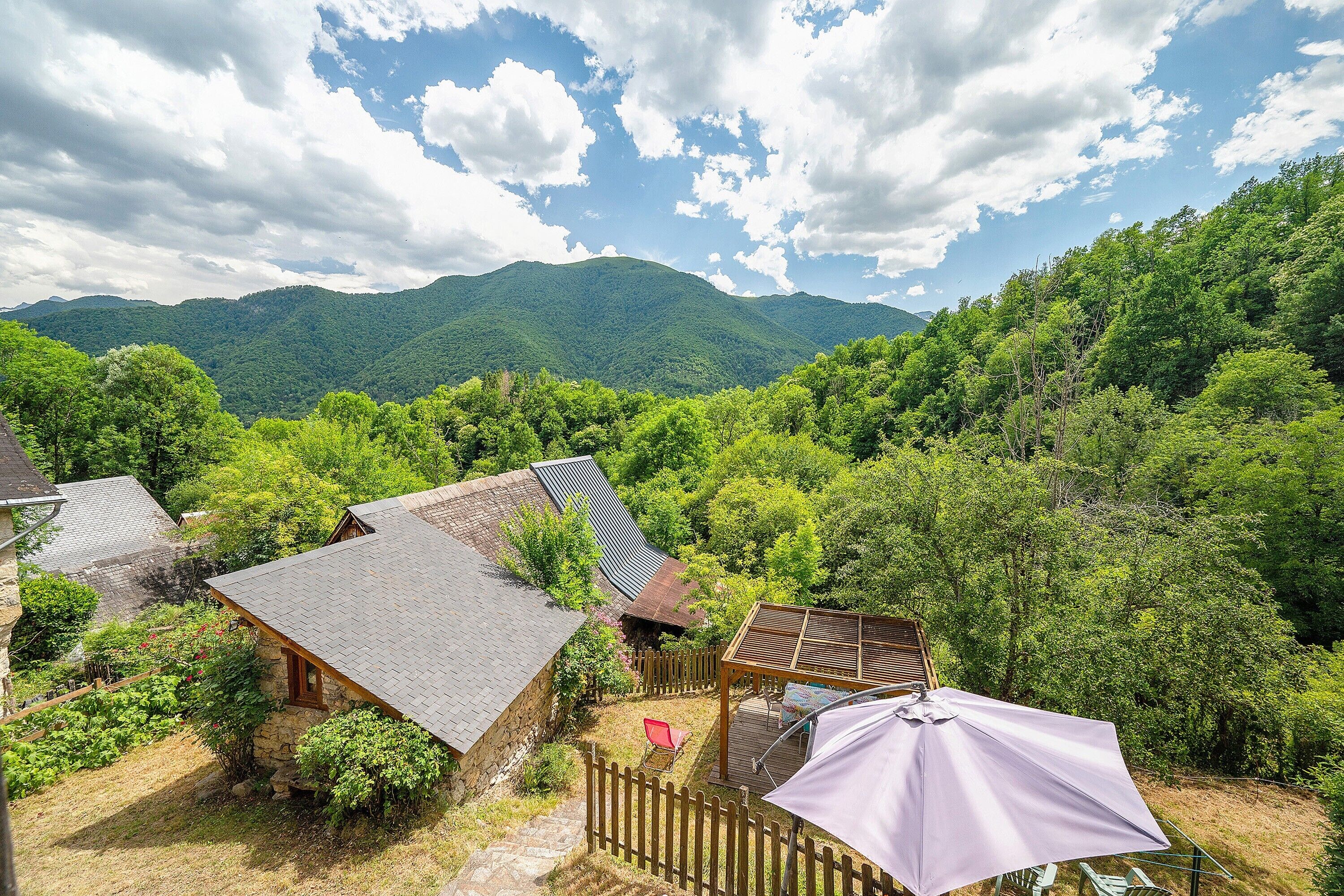 Une cabane rustique avec des fondations en pierre, une terrasse en bois et une pergola surmontée d’une tonnelle.