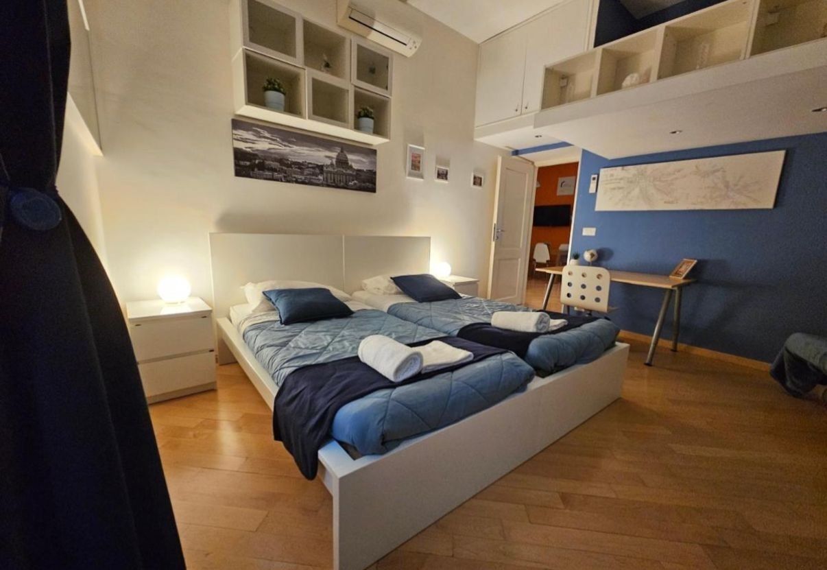 A bedroom with a bed, bedside tables, a wall-mounted shelf, and a door leading to another room.