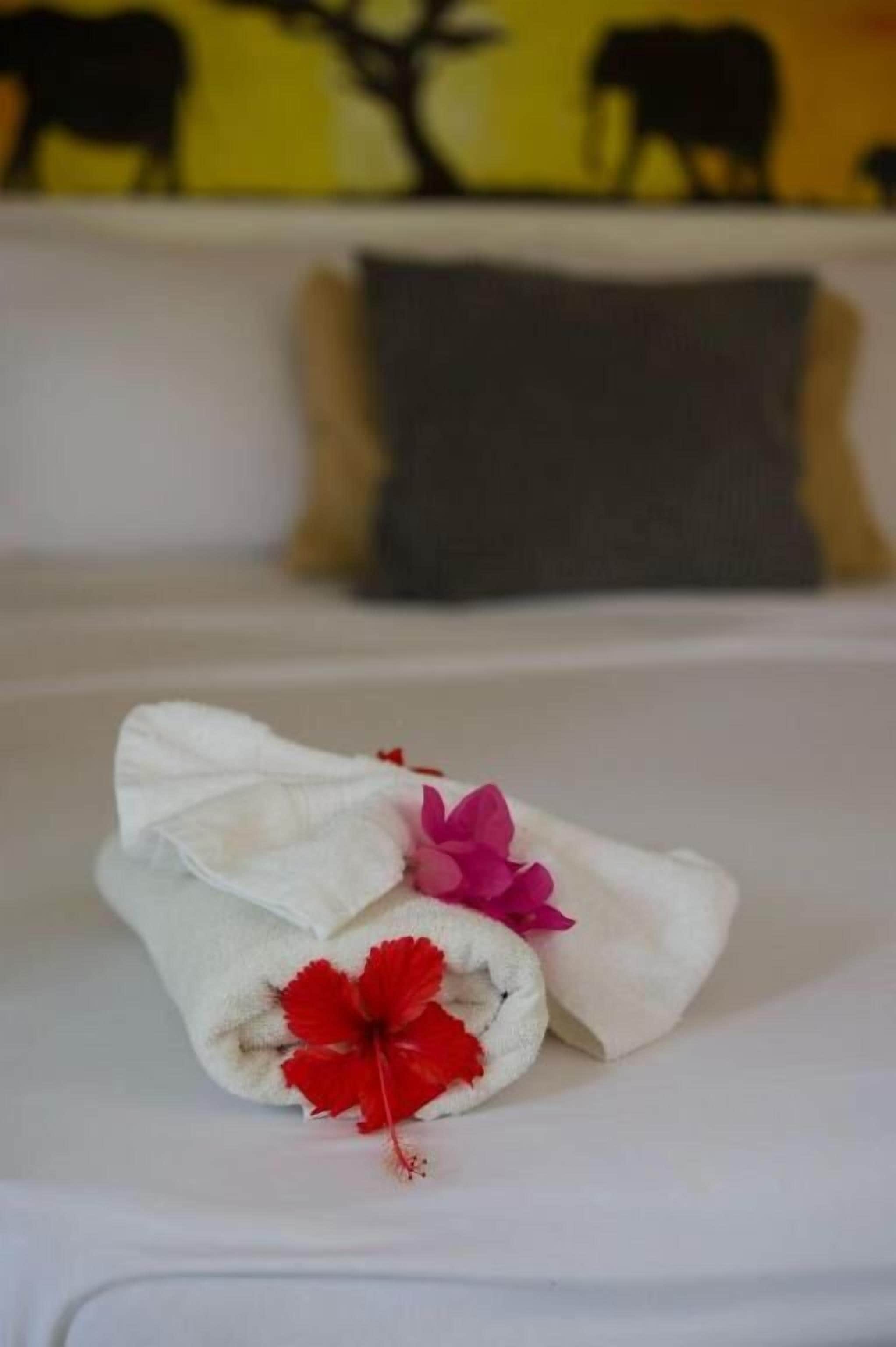 A bed with a white sheet, a gray pillow, and two towels with red flowers.